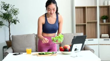 Formda bir Asyalı kadın dijital tablet kullanırken evde taze salata, meyve ve meyve suyu yiyor. Modern ev ortamında sağlık, beslenme ve canlılığın vücut bulmuş hali.