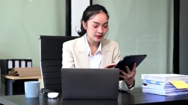 Modern ofis masasında dijital tablet ve dizüstü bilgisayar üzerinde çalışan başarılı Asyalı iş kadını