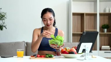 Formda bir Asyalı kadın dijital tablet kullanırken evde taze salata, meyve ve meyve suyu yiyor. Modern ev ortamında sağlık, beslenme ve canlılığın vücut bulmuş hali.