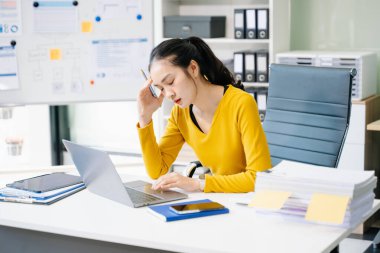 Modern ofiste dizüstü bilgisayarla çalışmaktan yorgun ve çok düşünen Asyalı bir kadın.