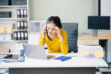 Modern ofiste dizüstü bilgisayarla çalışmaktan yorgun ve çok düşünen Asyalı bir kadın.