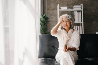 Bunalımda olan bir şişe haplı yaşlı kadın evdeki kanepede oturuyor.