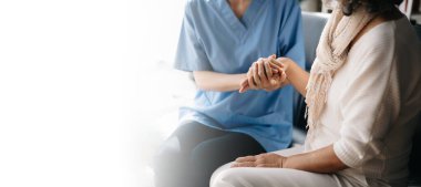 Bakıcı doktor yaşlı hastanın elini tutuyor, klinikteki kanepede oturuyor. Tıbbi servis kavramı