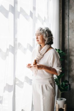 Depresyonda olan bir şişe haplı yaşlı kadın pencerede bekliyor.