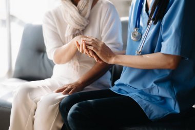Bakıcı doktor yaşlı hastanın elini tutuyor, klinikteki kanepede oturuyor. Tıbbi servis kavramı