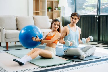 Evde enerjik egzersiz yapan çift yoga minderleri, spor aletleri ve hareketli aktif yaşam tarzını kullanıyor.