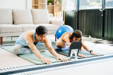 Çift evde enerjik egzersiz yapıyor, dijital tablet kullanıyor, yoga minderleri, spor aletleri ve hareketli aktif yaşam tarzı kullanıyor.