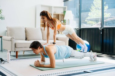 Evde enerjik egzersiz yapan çift yoga minderleri, spor aletleri ve hareketli aktif yaşam tarzını kullanıyor.