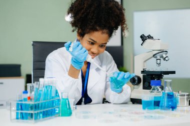 Bir tıp laboratuarında araştırma yapan genç Afrikalı Amerikalı bilim kadını mikroskop kullanıyor. Modern tıbbi araştırma laboratuvarı. 