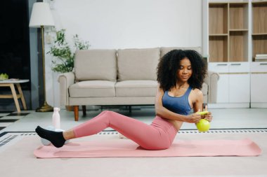 Modern bir ev ortamında kettlebell ile egzersiz yapan genç bir kadın. Sağlığını, motivasyonunu ve sağlıklı aktif bir yaşam tarzını gösteriyor.  