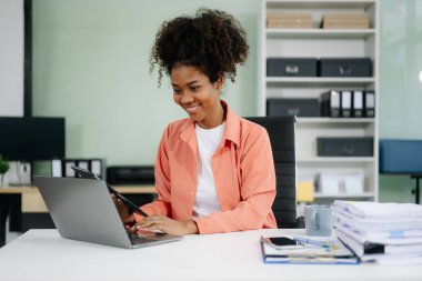 Genç Afrikalı Amerikalı iş kadını modern ofiste dizüstü bilgisayar ve tabletle çalışıyor. 