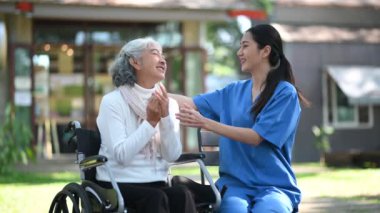 Hastane bahçesinde Asyalı yaşlı bir kadınla ilgilenen ve konuşan genç bir hemşire.