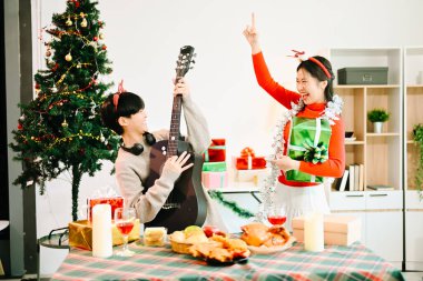 Couple enjoying of Christmas holidays exchanging gifts and playing guitar with festive decorations at home clipart