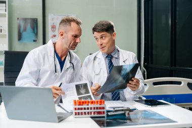 Doktorlar röntgeni inceliyor, tıbbi bir ofiste dijital aletlerle işbirliği yapıyorlar. Hasta bakımı için takım çalışması, teşhis ve sağlık uzmanlığı