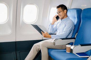 Akıllı telefonda konuşurken rahat koltukta oturan Asyalı erkek yolcu. Stil içinde seyahat et, zarafetle çalış.