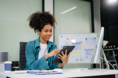 Genç ve güzel bir kadın çalışma yerinde otururken tablet kullanıyor. İşine odaklan..