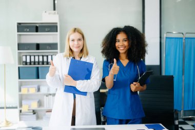 Doktor ve hemşire dijital tablet tutuyorlar ve modern hastanede başparmaklarını gösteriyorlar. 