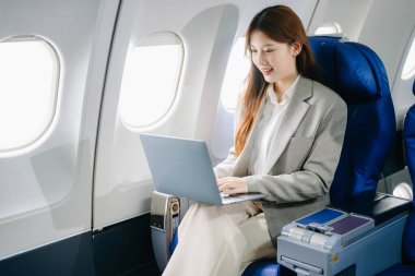 Asyalı bir kadın birinci sınıf uçak koltuğunda ve dizüstü bilgisayar kullanıyor. Lüks, konfor ve zarafet sergiliyor. Havacılık, turizm ve iş hayatı için mükemmel. 