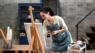Kadın ressam sanat atölyesinde resim yapıyor, resim malzemeleri, yağlı boya tabloları, tuval sehpası, resim stüdyosunda veya oturma odasında fırçalı yaratıcı alanlar..