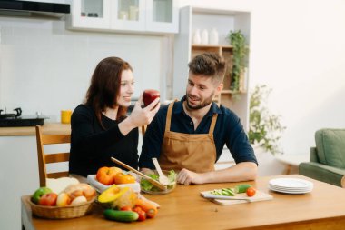 Neşeli bir çift keşfedin taze sebzeler hazırlayan, sağlıklı beslenmeyi kucaklayan ve canlı bir mutfak ortamında takım çalışması yapan. Sağlıklı yaşam tarzı için mükemmel.