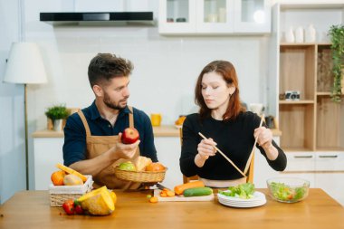 Evde yemek yapan bir çift. Genç çift ekmek ve taze sebzelerle birlikte yemek pişiriyor, sıcacık mutfakta sağlıklı besleniyorlar. Sağlıklı yaşam tarzı için mükemmel. 