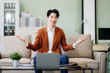 Asyalı girişimci işine odaklanmış, şık bir ofiste koltukta dizüstü bilgisayarla belgeleri analiz ediyor. İş için mükemmel, verimlilik için.