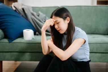 Depresyondaki Asyalı kadın oturma odasında kanepede oturmaktan endişe duyuyor. Hastalık, sağlık ve iyileşme kavramı.