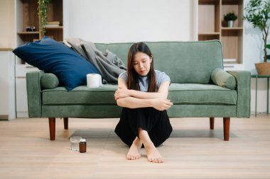 Depresyondaki Asyalı kadın oturma odasında kanepede oturmaktan endişe duyuyor. Hastalık, sağlık ve iyileşme kavramı.