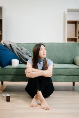 Depresyondaki Asyalı kadın oturma odasında kanepede oturmaktan endişe duyuyor. Hastalık, sağlık ve iyileşme kavramı.