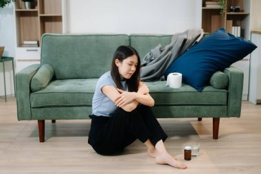 Depresyondaki Asyalı kadın oturma odasında kanepede oturmaktan endişe duyuyor. Hastalık, sağlık ve iyileşme kavramı.