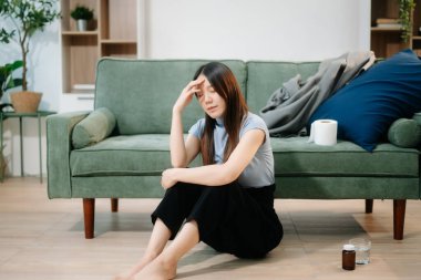 Depresyondaki Asyalı kadın oturma odasında kanepede oturmaktan endişe duyuyor. Hastalık, sağlık ve iyileşme kavramı.