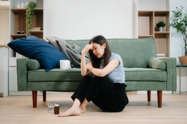 Depresyondaki Asyalı kadın oturma odasında kanepede oturmaktan endişe duyuyor. Hastalık, sağlık ve iyileşme kavramı.