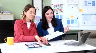 Ofiste birlikte çalışan iki iş kadını, akıllı telefon ve dizüstü bilgisayar kullanarak yeni bir proje yürütüyorlar. 