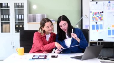 Ofiste birlikte çalışan iki iş kadını yeni bir proje yürütüyor ve dizüstü bilgisayar kullanıyor. 