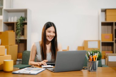 Genç işyeri sahibi kadın paket kutusunu hazırla ve tablet, dizüstü bilgisayar alışverişi online konsept üzerinden müşteriye teslimat için çevrimiçi kontrol yap.