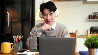 Genç Asyalı adam kulaklıkla müzik dinlerken dizüstü bilgisayar ve tablet kullanıyor.