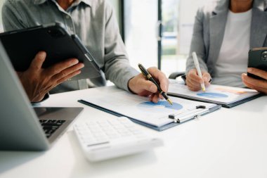 Akıllı telefon ve hesap makinesi olan ofis masasındaki iş belgeleri dijital tablet ve sosyal ağ diyagramı olan grafik işleri ve büroda çalışan verileri tartışan iki meslektaş