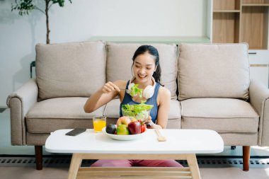  Formda bir kadın taze salatadan meyve ve meyve suyu, sağlıklı yaşam, beslenme ve zindelik dolu parlak, modern bir ev ortamında keyif alır. Sağlıklı bir yaşam tarzı!