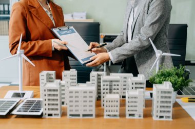 Modern bir ofisteki Asyalı mimar ve geliştiriciler, yenilikçi ve emlak planları tasarlamak için yapı modelleri ve dijital araçları kullanarak işbirliği yaparlar.