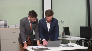 İki ofis arkadaşı, dizüstü bilgisayar kullanarak modern bir çalışma alanında yeni bir proje için fikir alışverişinde bulunuyor.                       