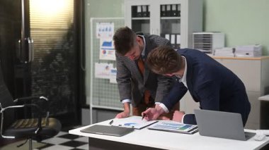 İki ofis arkadaşı, dizüstü bilgisayar kullanarak modern bir çalışma alanında yeni bir proje için fikir alışverişinde bulunuyor.                       