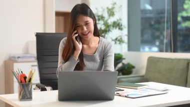 İş kadını akıllı telefonla konuşuyor ve ofis masasında dizüstü bilgisayar kullanıyor, vergi raporları yazıyor ve analitik araştırmalar yapıyor.