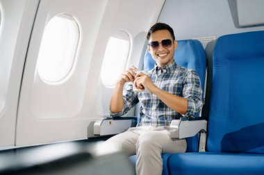 Uçakta bir koltukta oturan ve pencereden dışarı bakan Asyalı bir adam seyahate çıkıyor.