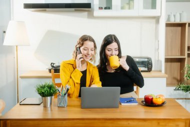 Mutfak masasında laptopla ve akıllı telefonuyla çalışan iki beyaz kadın.. 