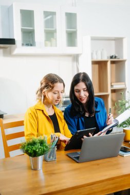 Beyaz kadınlar mutfak masasında oturup laptopla tablet üzerinde çalışıyorlar.. 
