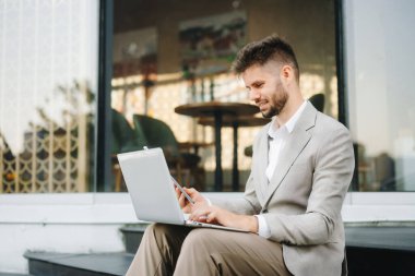 Başarılı iş adamı ofis yakınlarında çalışıyor. Güneş ışığında bir tablet ve akıllı telefon tutuyor.