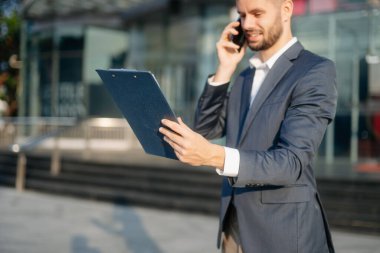 Modern iş adamı akıllı telefondan konuşuyor ve şehirdeki iş merkezinde pano tutuyor.