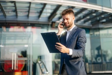 Modern iş adamı akıllı telefondan konuşuyor ve şehirdeki iş merkezinde pano tutuyor.