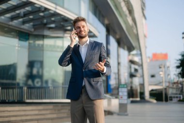 Modern iş adamı şehirdeki iş merkezinde akıllı telefondan konuşuyor.