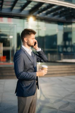 Modern iş adamı akıllı telefondan konuşuyor ve şehirdeki iş merkezinde kahve içiyor.